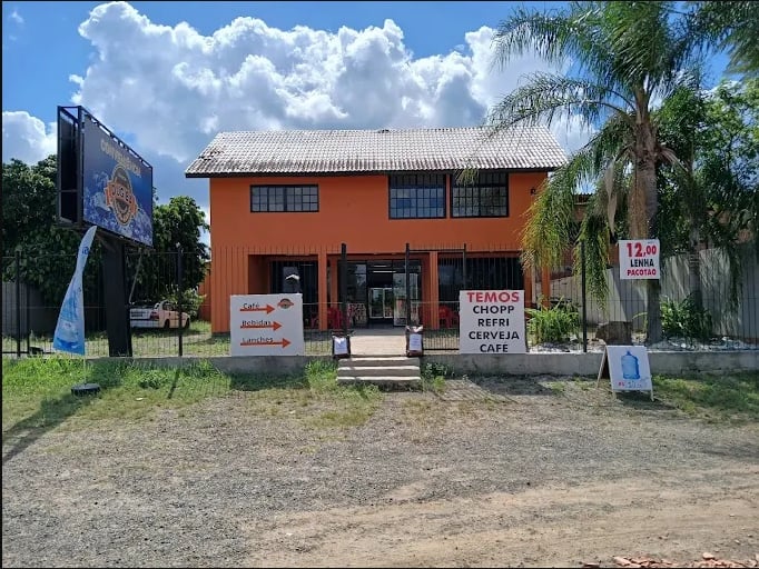 Entrada da loja de conveniência DUGIBA. Prédio laranja com placas de sinalização de produtos e servi
