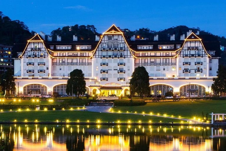Fachada iluminada do Palácio Quitandinha refletida no lago ao anoitecer em Petrópolis.