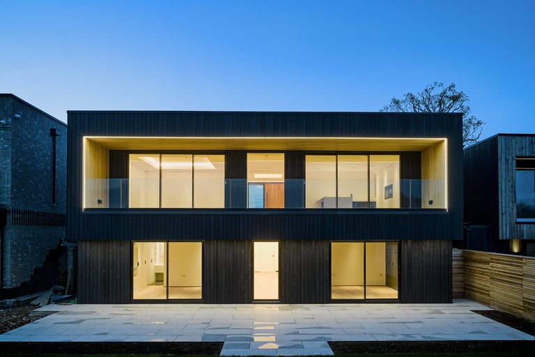 Modern black timber clad house with illuminated glass balconies and large windows at dusk.