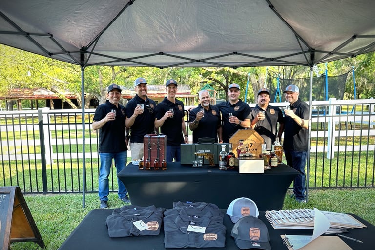 Bullets & Bourbon members standing together holding glasses of bourbon behind a table of different bourbon bottles