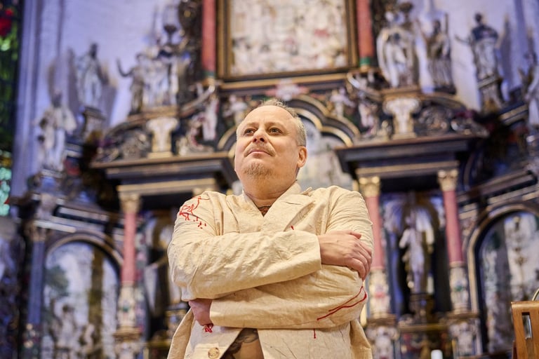 Ein Schauspieler vor einem Altar mit den Armen vor dem Körper.