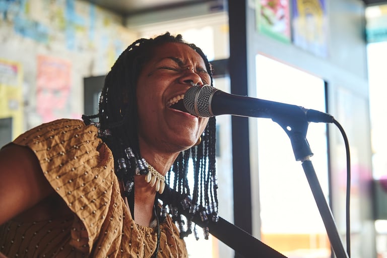 A soulful female singer with braided hair performing live into a microphone during a concert.