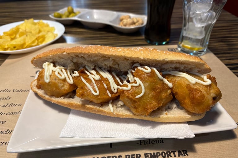 Spanish calamari sandwich with garlic aioli served with potato chips, olives, and a cold drink.