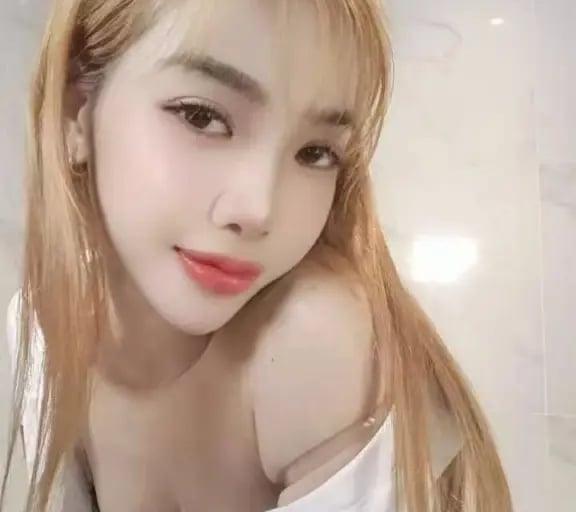A blonde woman with red lipstick posing in a white button-down shirt in a modern bathroom.