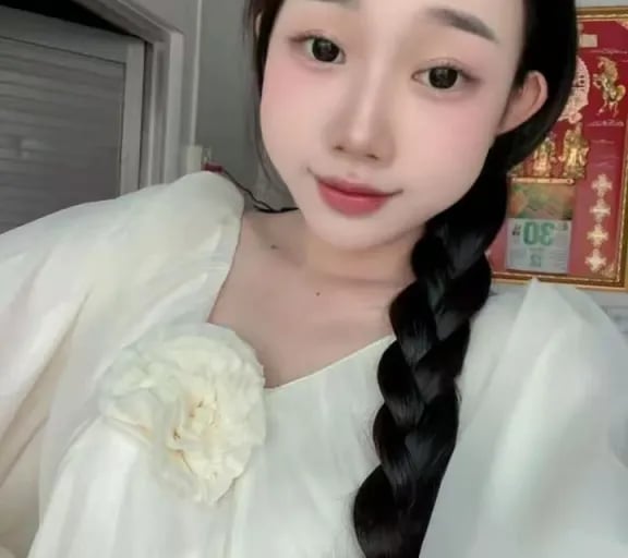 Young woman with long black braided hair wearing a white blouse with a floral brooch and a cute cookie hair clip.