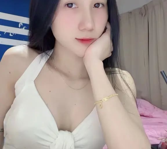 Young woman with long dark hair wearing a white halter top posing indoors at a marble table.