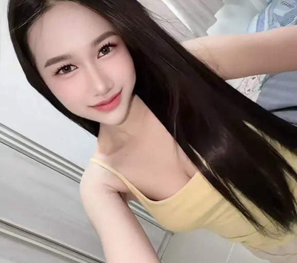 Smiling woman with long straight black hair wearing a yellow tank top in a bright room.