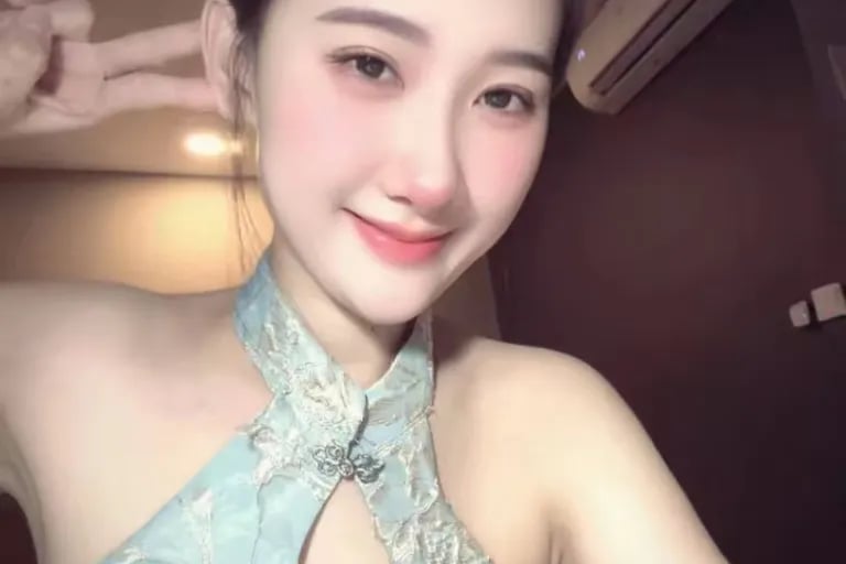 A smiling young Asian woman in a light blue floral halter dress making a peace sign.