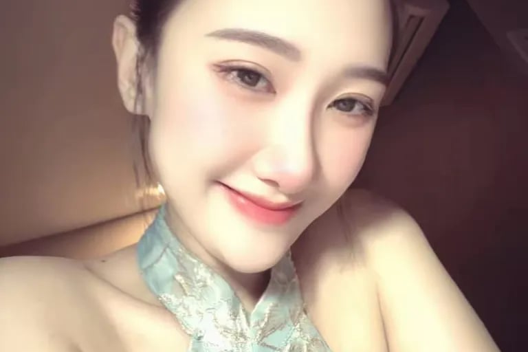 Smiling woman with her hair in a bun wearing a light blue halter dress with floral embroidery.