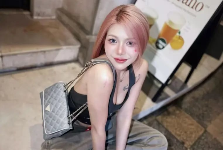 A stylish young woman with pink hair wearing cargo pants and a designer shoulder bag posing outdoors.