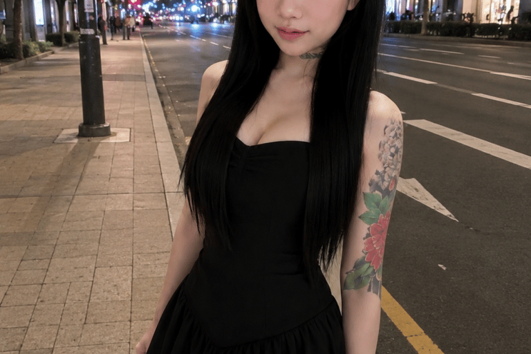 Young woman with long black hair and a floral arm tattoo wearing a black dress on a city street at night.