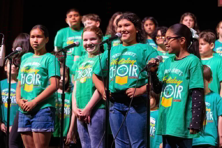 Merced Children's Holiday Choir performing in green t-shirts during a musical concert on stage.
