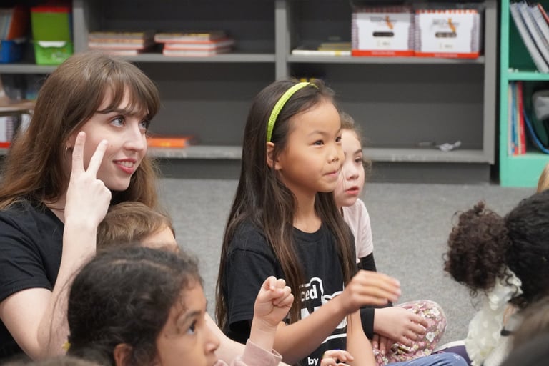 A teacher and diverse elementary students learning sign language in a classroom setting.