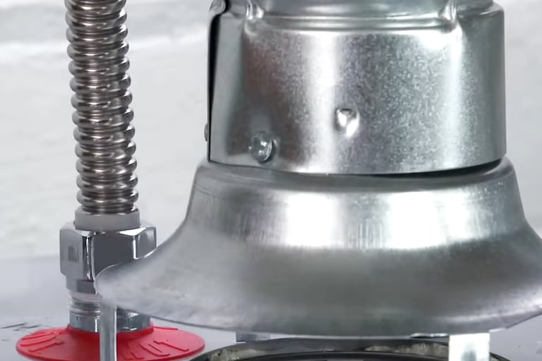 Close-up of a gas water heater draft hood and flexible gas line connector.