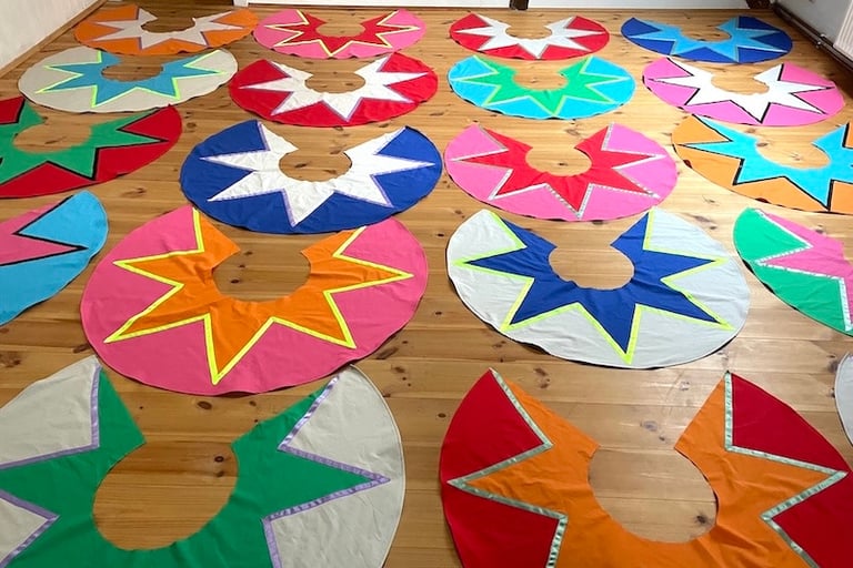 Handmade colorful circus costumes with star patterns laid out on a wooden floor.