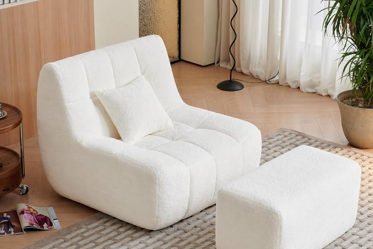 Modern white boucle accent chair with matching ottoman on a textured rug in a cozy living room.