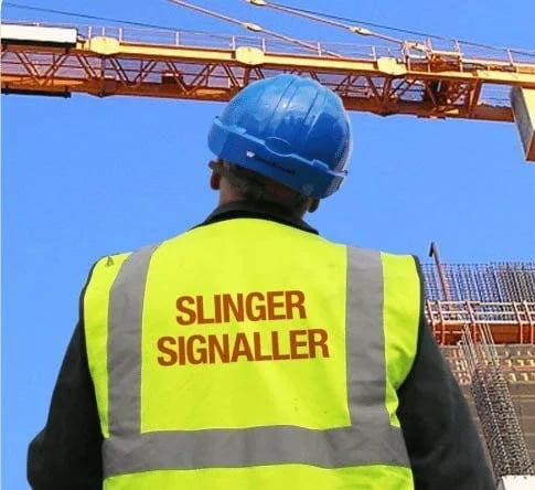 A slinger signaller in a high-visibility vest and blue hard hat monitoring a construction crane.