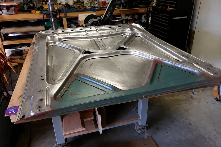 A custom steel car hood restoration project on a metal workbench in a professional garage.