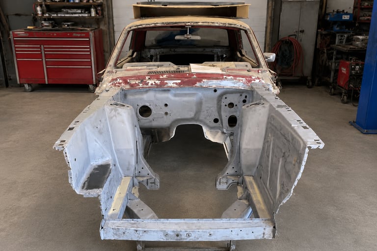A vintage classic car frame undergoing restoration in an auto body repair shop.