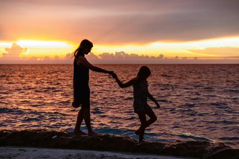Madre e hija caminando por la playa tomadas de la mano