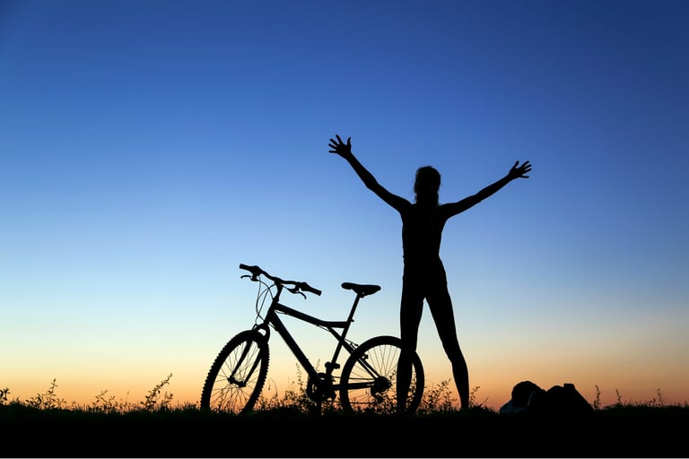 Mujer en bici mirando al firmamento mientras levanta los brazos