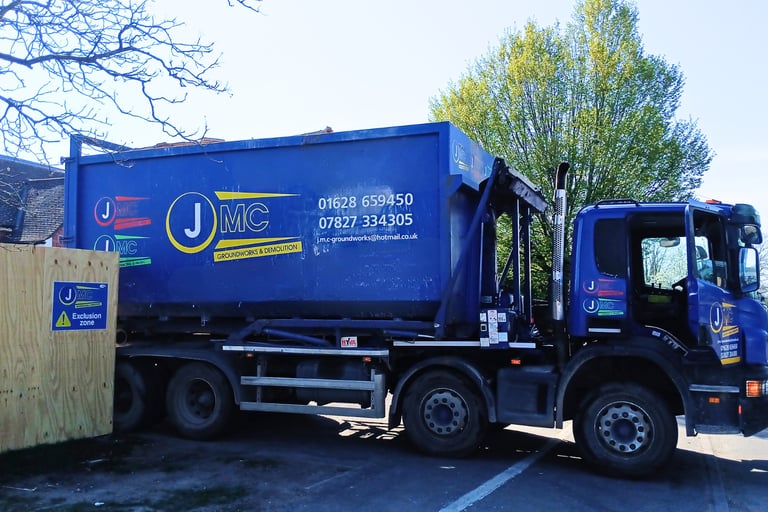 Blue JMC Groundworks and Demolition skip loader truck parked at a construction site.