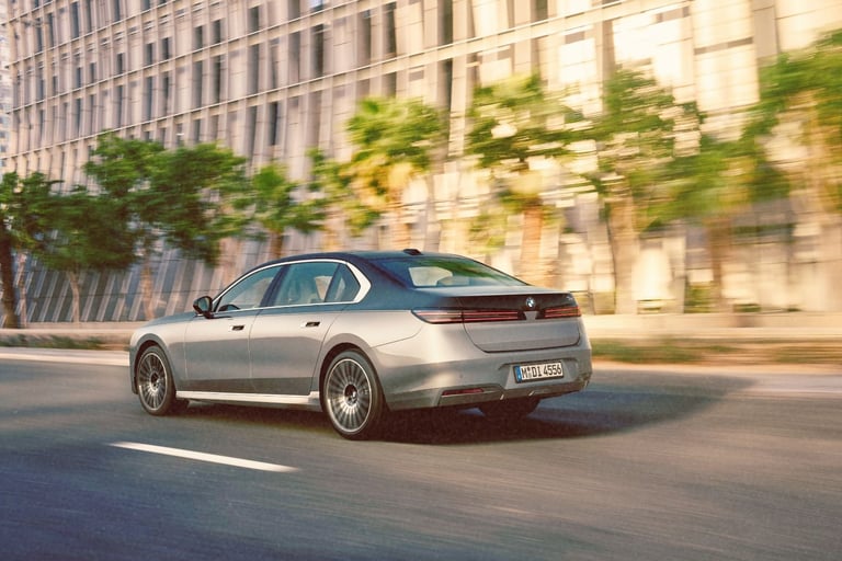 Luxury BMW i7 electric sedan in two-tone grey driving on a modern city street with palm trees.