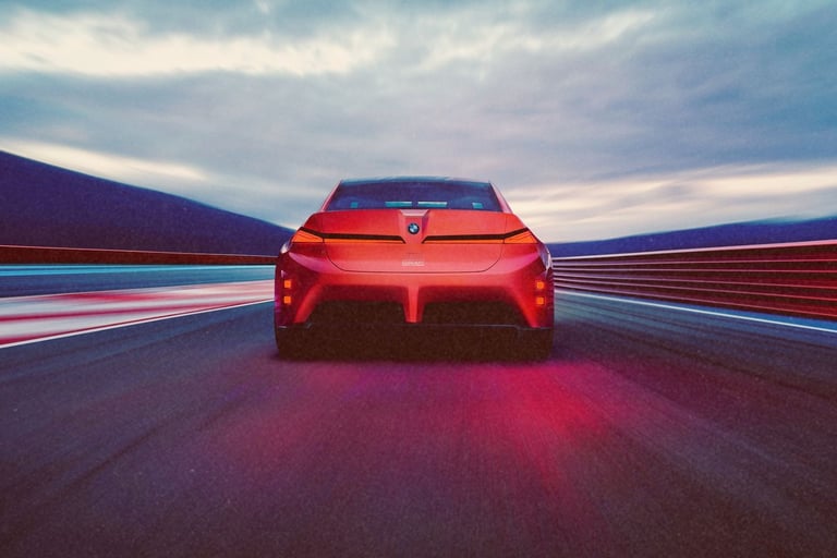 Rear view of a red BMW concept electric car driving on a high-speed racetrack at dusk.