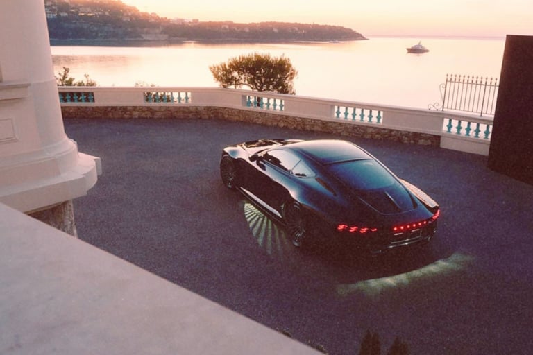 Black luxury sports car parked on a scenic coastal driveway overlooking the ocean at sunset.