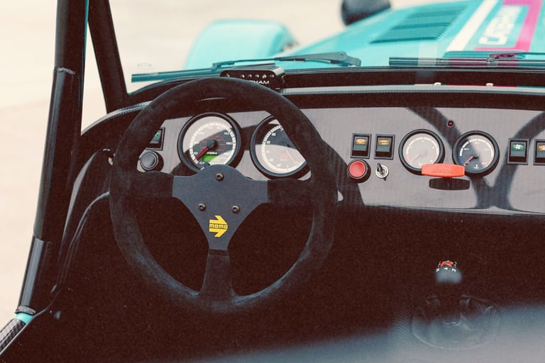 Interior view of a Caterham sports car featuring a Momo steering wheel and carbon fiber dashboard gauges.