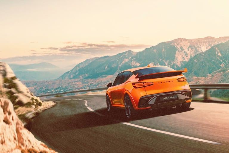 An orange Genesis GV60 Magma performance electric SUV driving on a winding mountain road.