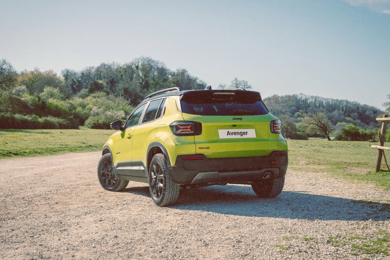 A lime green Jeep Avenger 4xe compact SUV parked on a gravel path in a sunny outdoor countryside setting.