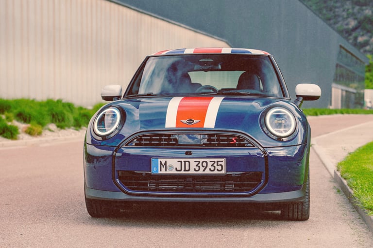 Front view of a blue Mini Cooper S with white and red racing stripes parked on a road.