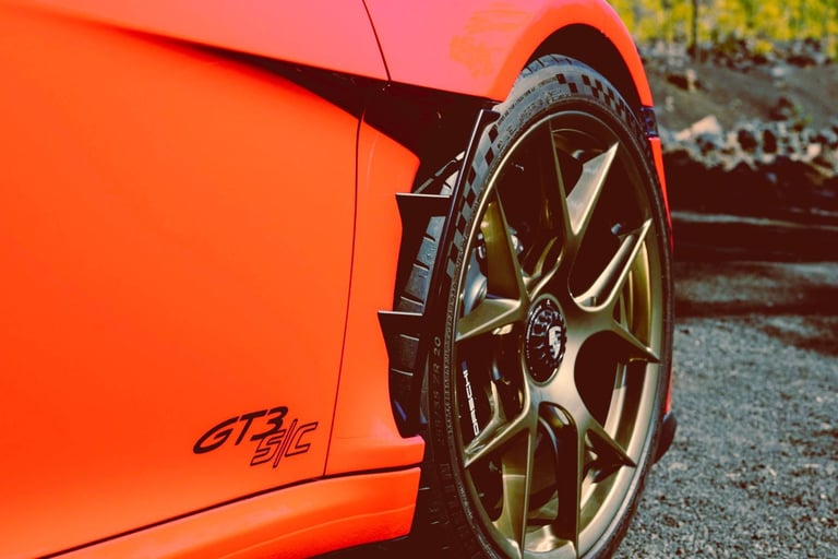 Close-up of an orange Porsche GT3 S/C fender and gold alloy wheel with high-performance tires.
