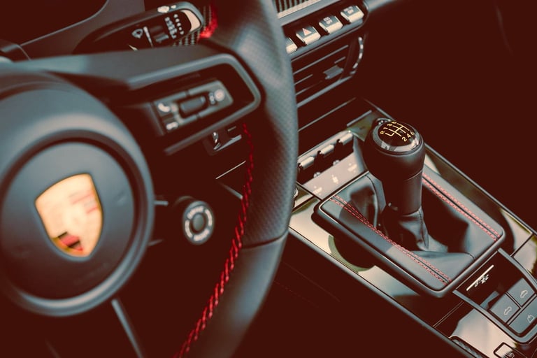 Close-up of a Porsche interior featuring a manual gear shifter and leather steering wheel with red stitching.