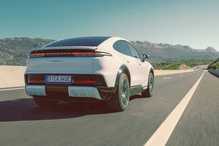 A white Porsche Cayenne S E-Hybrid Coupe driving on a highway with mountain views.