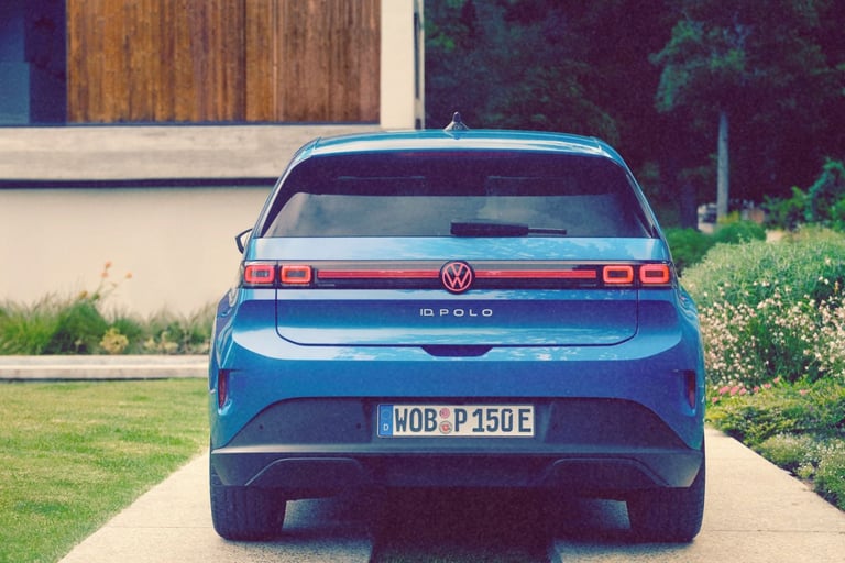 Rear view of a blue Volkswagen ID. Polo electric car parked on a driveway near a garden.