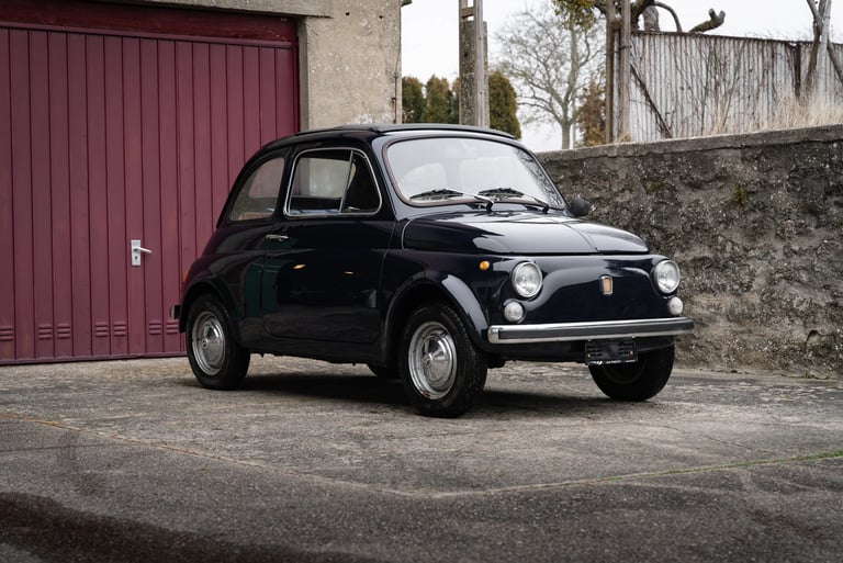 a fiat 500 parked in front of a red garage door