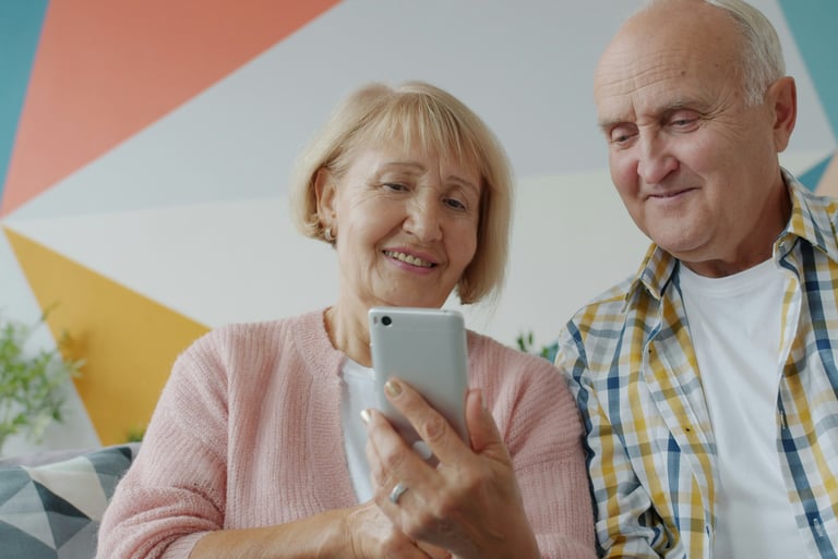 A happy senior couple sitting together on a couch while using a smartphone for a active aging