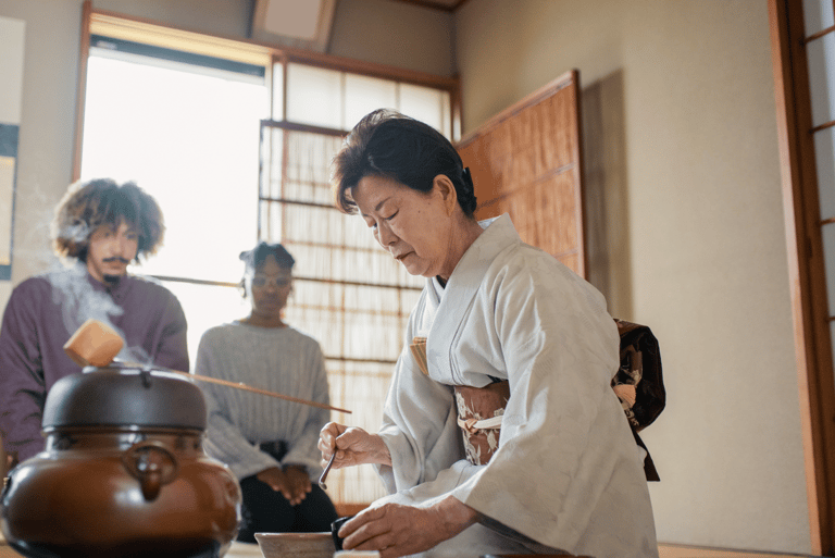woman wearing a kimono performs tea ceremony and tourists watching in the back