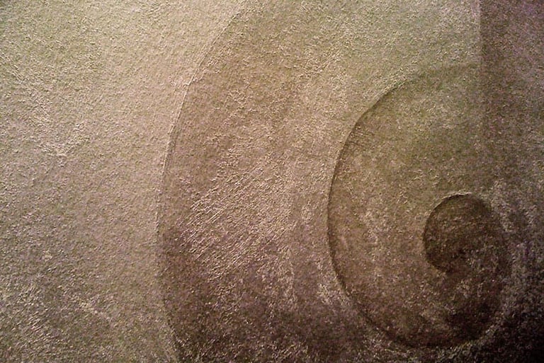 Close-up of a snail swirl painted with warm silver paint in a gritty texture.
