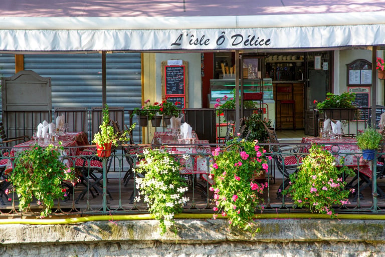 Outdoor patio at L'isle O Delice restaurant with floral decorations and red checkered tablecloths.