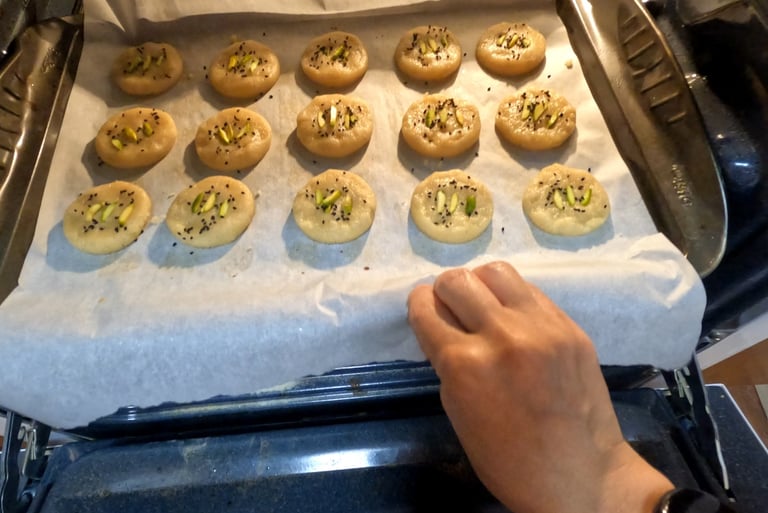 Round cookies with pistachios and seeds on a tray being placed into the oven