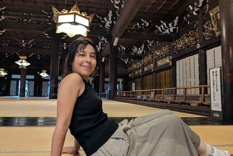 Woman sitting inside Nishi Hongan-ji Temple in Kyoto, surrounded by wooden pillars and tatami flooring.