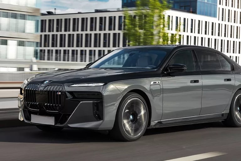 A two-tone grey and black BMW 7 Series luxury sedan driving on a city road with modern buildings in the background.