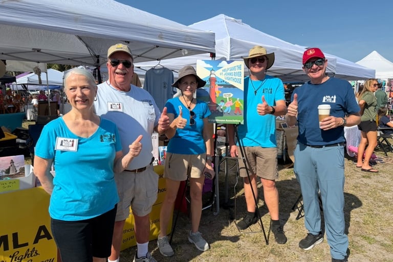 MLA Volunteers give the camera a cheery thumbs-up as they stand in front of the MLA market booth.