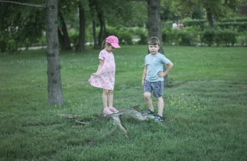 A boy and girl standing beside trees, exploring a wooded area during daytime.