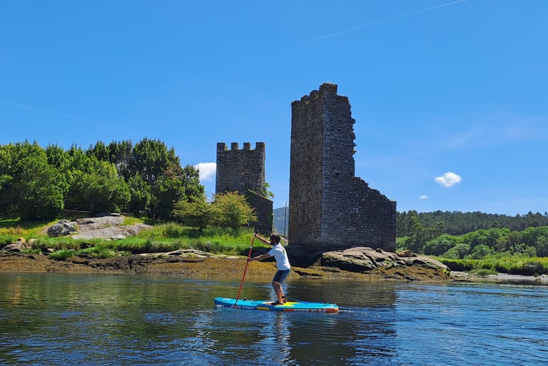 Chico remando con un paddle surf frente a las torres del oeste de Catoira