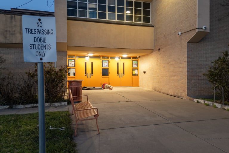 Homeless person sleeping by doors of a school next to a no trespassing sign