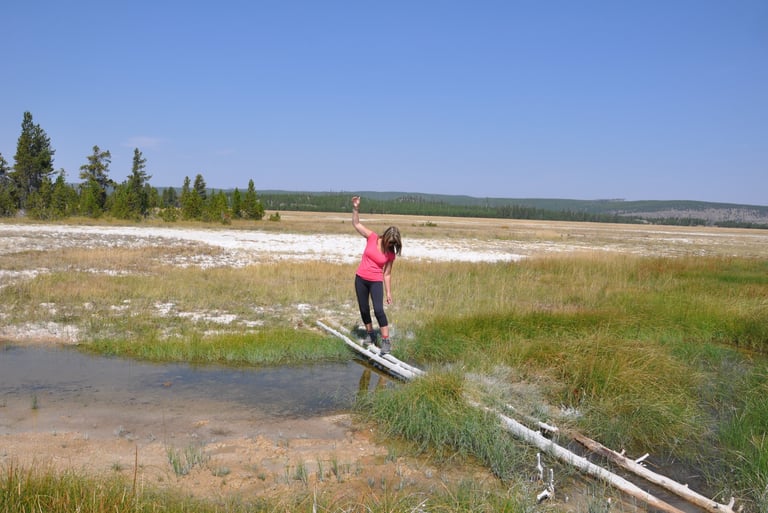 a woman standing on a log bridge over fairy creek, Yellowstone national park